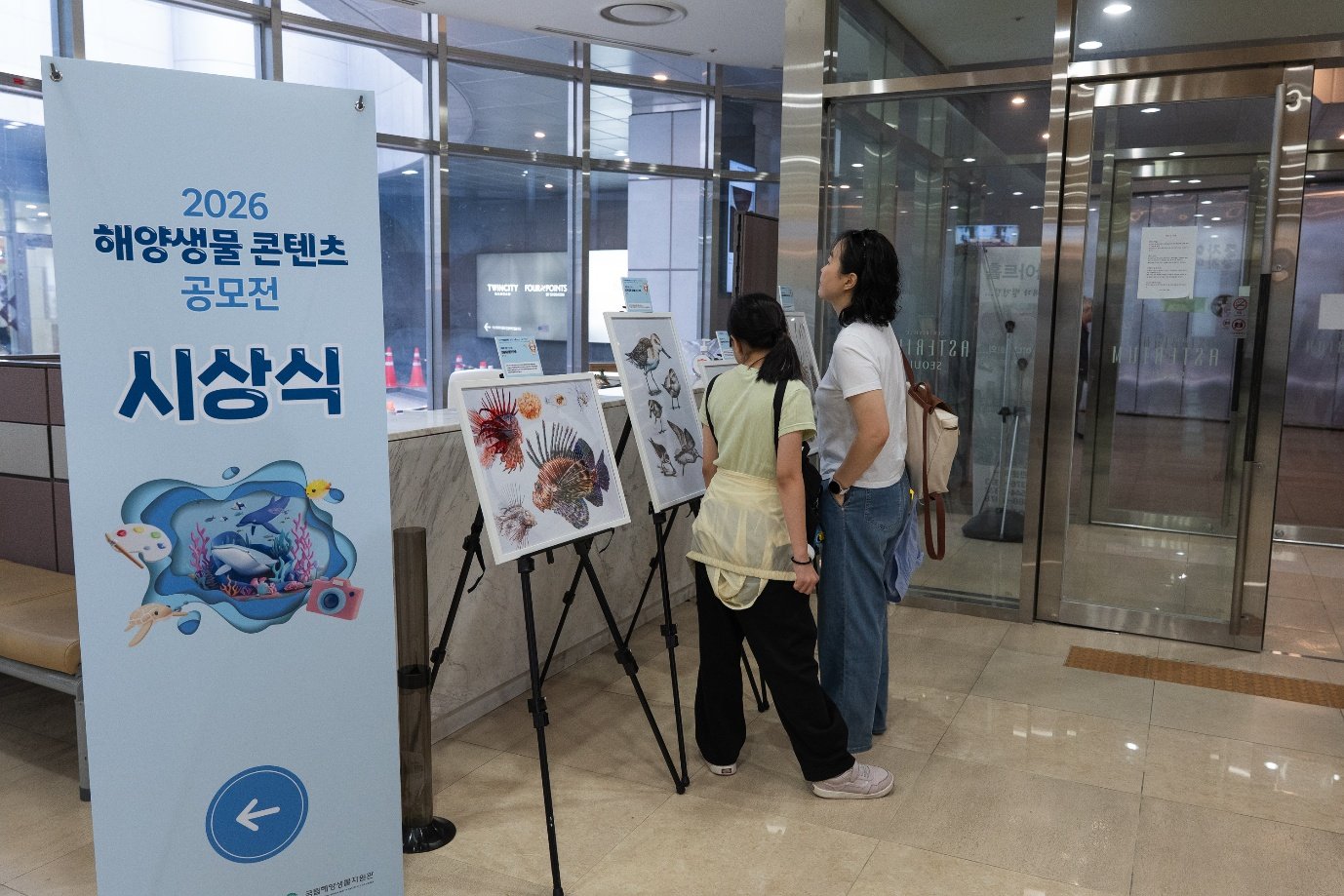 로비 전시 공간에서 공모전 수상작을 감상하는 관람객